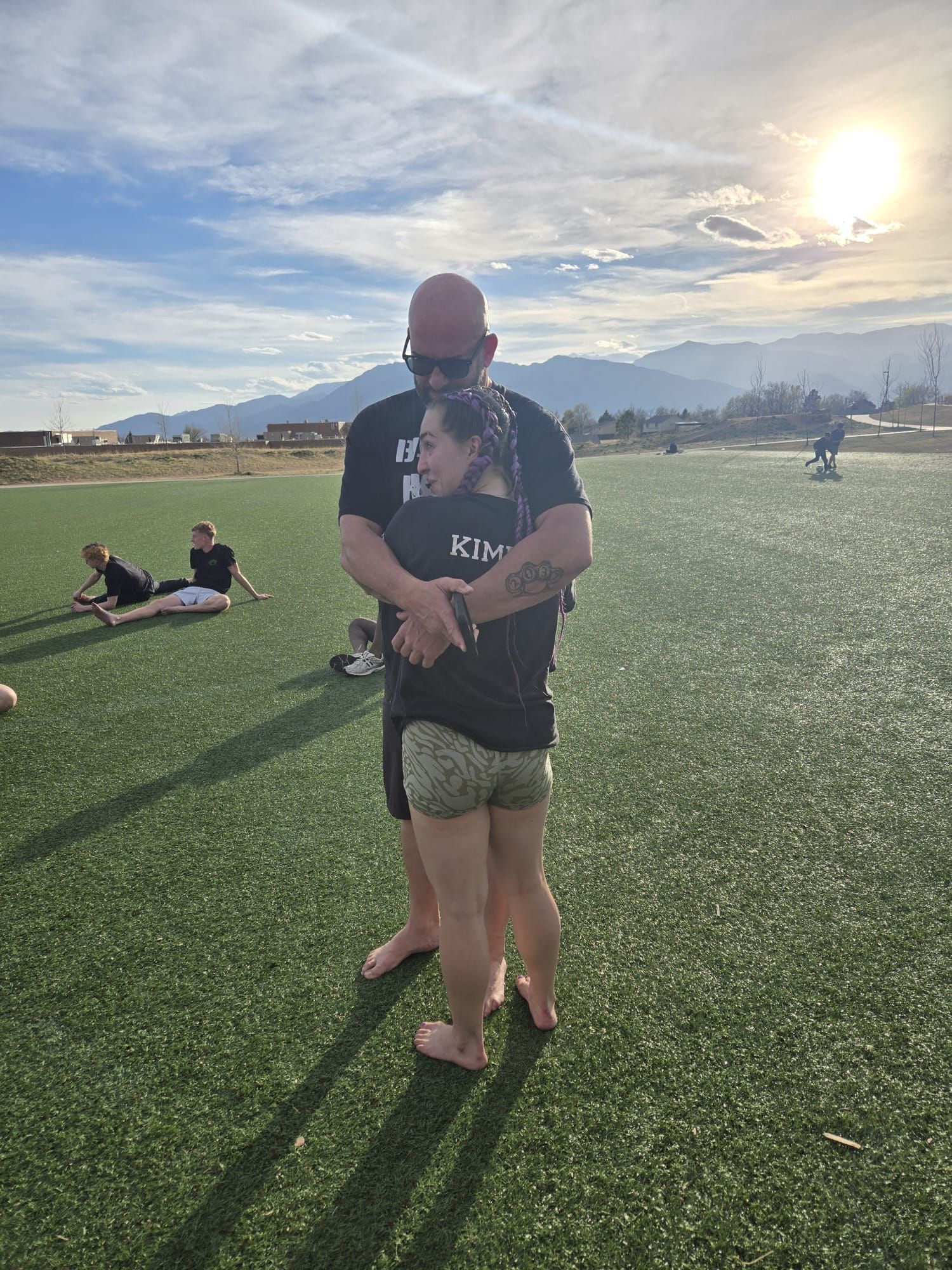 Coach hugging Kimie after a hard session on the soccer field at sunset, Colorado mountains in the background