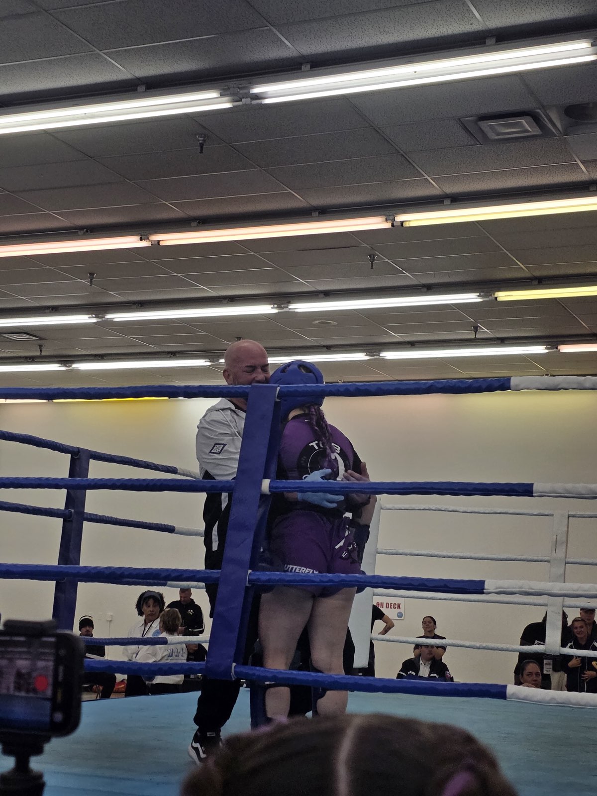 Papa Pit hugging a TCB female fighter in blue headgear at the corner of the ring after her bout at the 2026 WAKO USA Nationals