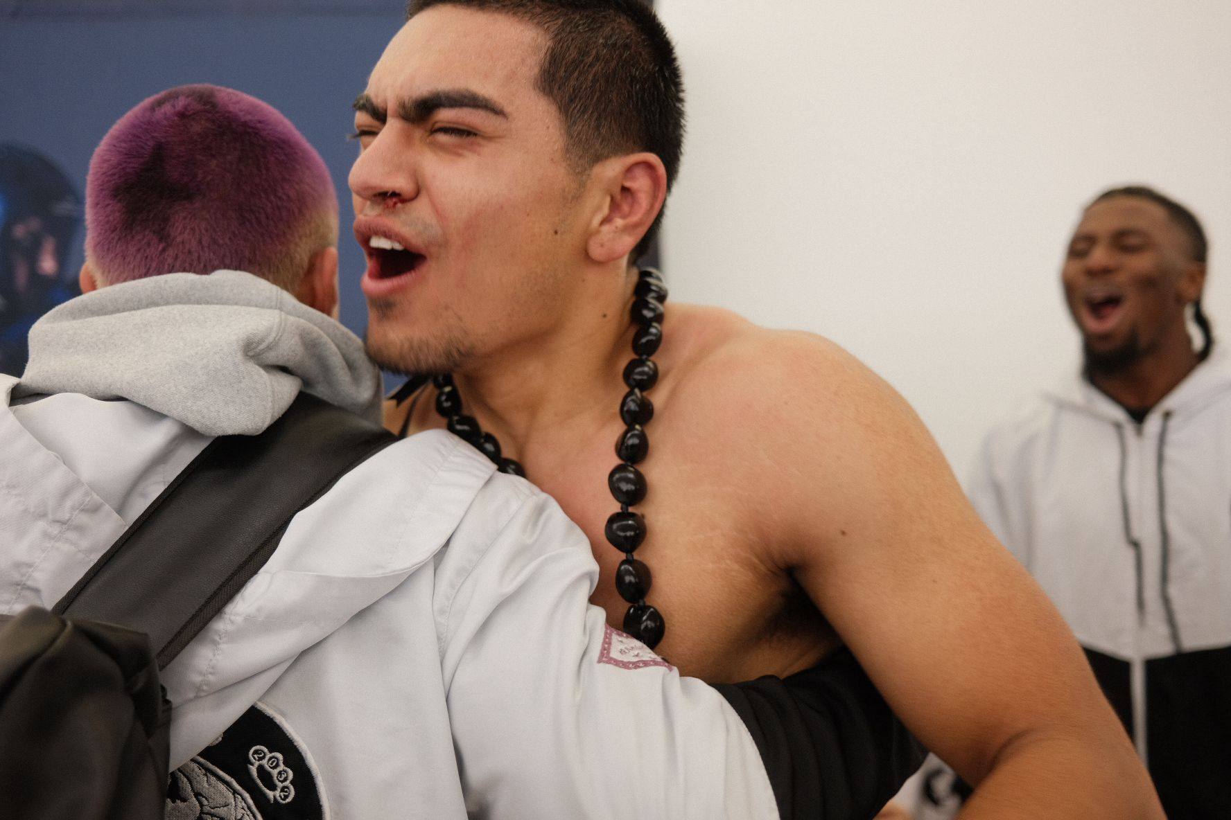 TCB fighter embracing teammate after his WAKO USA bout, the room erupting around them