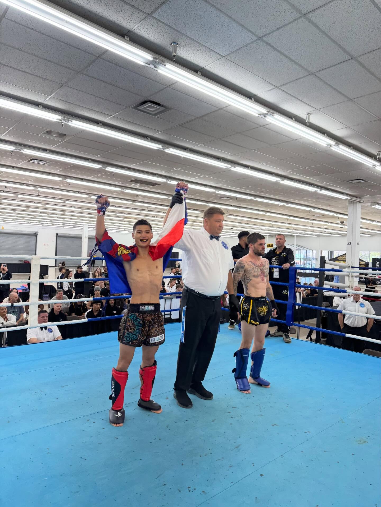 TCB fighter wrapped in a flag with arms raised in victory, referee holding his wrist after a win at the 2026 WAKO USA Nationals