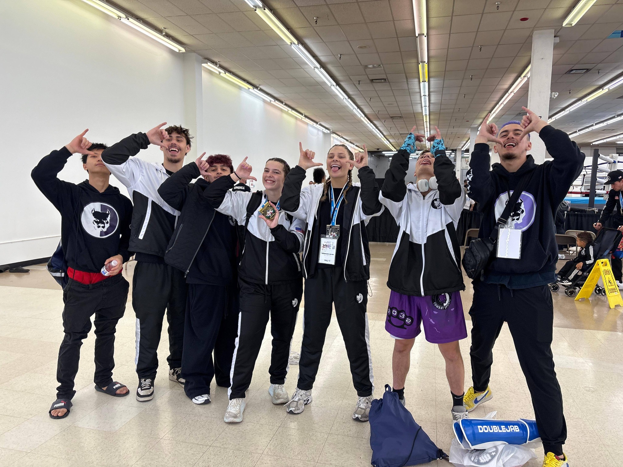 TCB fighters in matching black-and-white tracksuits celebrating after a WAKO USA win