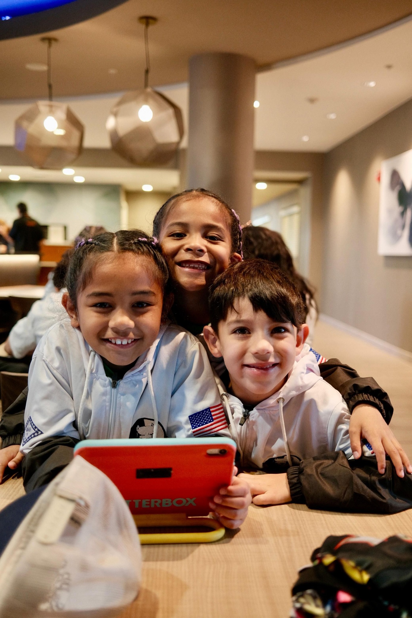 Three young TCB kids in matching team jackets with Arkansas patches smiling at the WAKO USA hotel