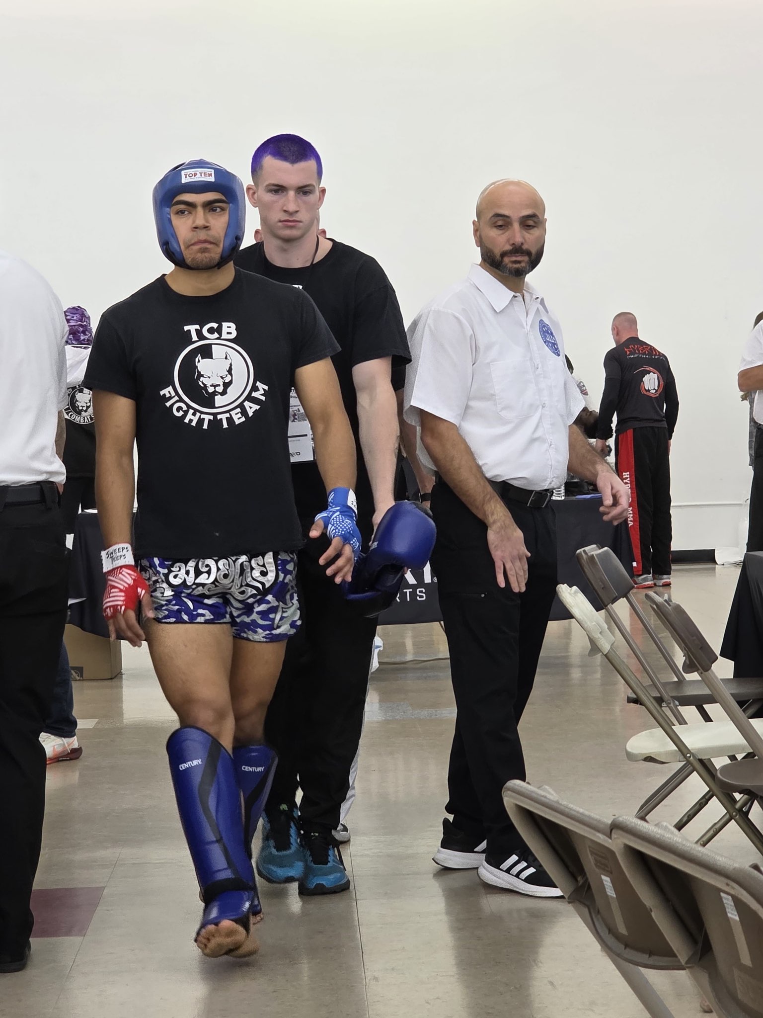 A TCB Fight Team fighter walking out toward the ring with shin guards laced and corner team behind him at the 2026 WAKO USA Nationals