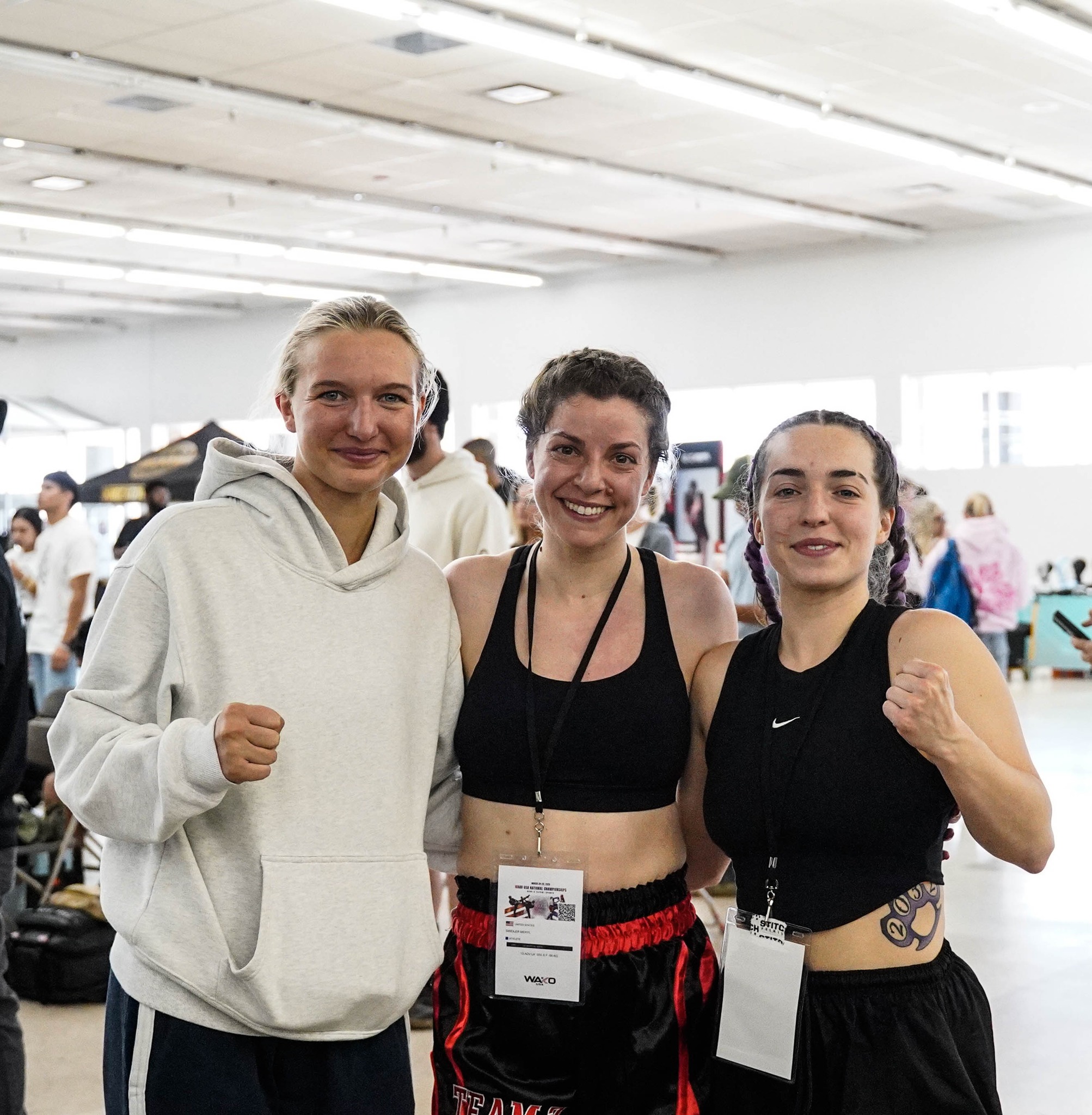 Three TCB female fighters posing together with fists raised at the 2026 WAKO USA Nationals venue
